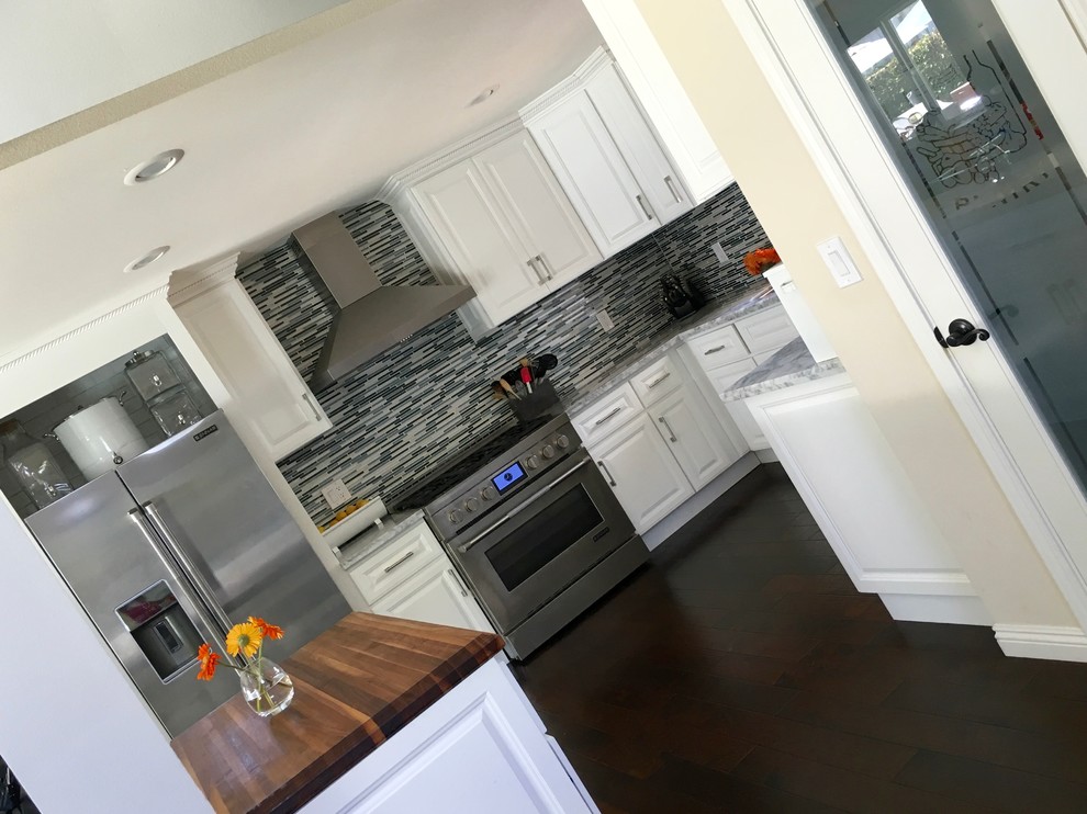 Example of a mid-sized transitional dark wood floor eat-in kitchen design in Orange County with raised-panel cabinets, white cabinets, wood countertops, blue backsplash, matchstick tile backsplash, stainless steel appliances and an island