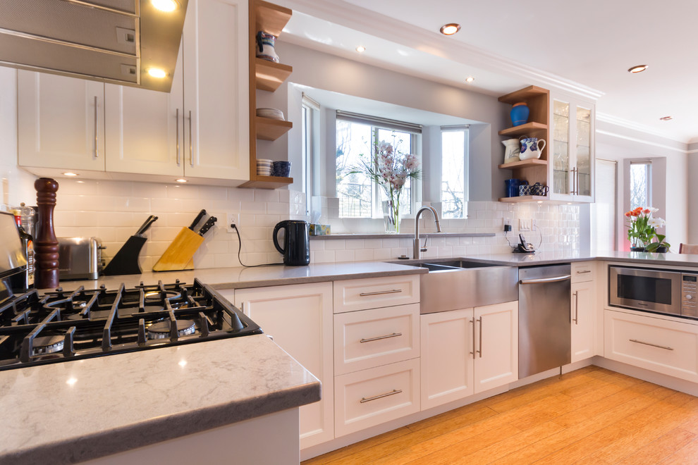 Design ideas for a medium sized traditional u-shaped enclosed kitchen in Vancouver with a belfast sink, shaker cabinets, white cabinets, quartz worktops, white splashback, metro tiled splashback, stainless steel appliances, bamboo flooring, a breakfast bar and brown floors.