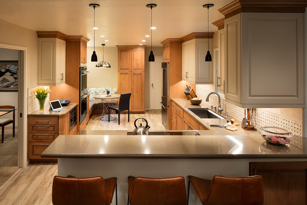 This is an example of a traditional l-shaped kitchen/diner in San Francisco with a single-bowl sink, raised-panel cabinets, medium wood cabinets, engineered stone countertops, beige splashback, travertine splashback, stainless steel appliances, vinyl flooring, a breakfast bar and beige floors.