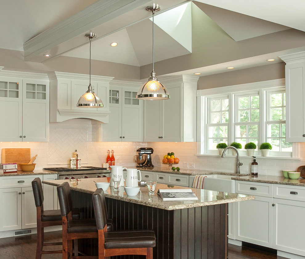 Example of a mid-sized classic l-shaped medium tone wood floor eat-in kitchen design in Philadelphia with a farmhouse sink, shaker cabinets, white cabinets, granite countertops, white backsplash, ceramic backsplash, stainless steel appliances and an island