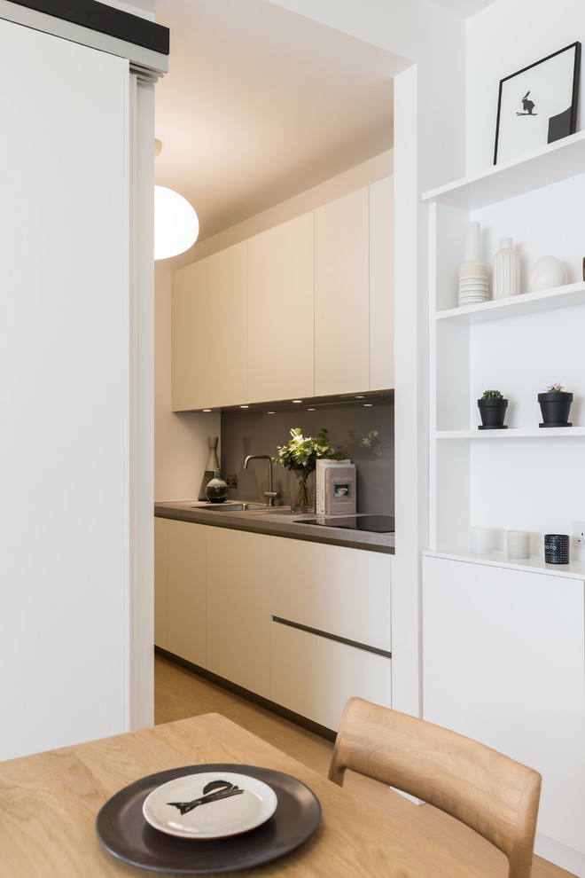 Foto på ett mellanstort funkis kök, med en enkel diskho, släta luckor, vita skåp, integrerade vitvaror, laminatbänkskiva, grått stänkskydd, glaspanel som stänkskydd och ljust trägolv