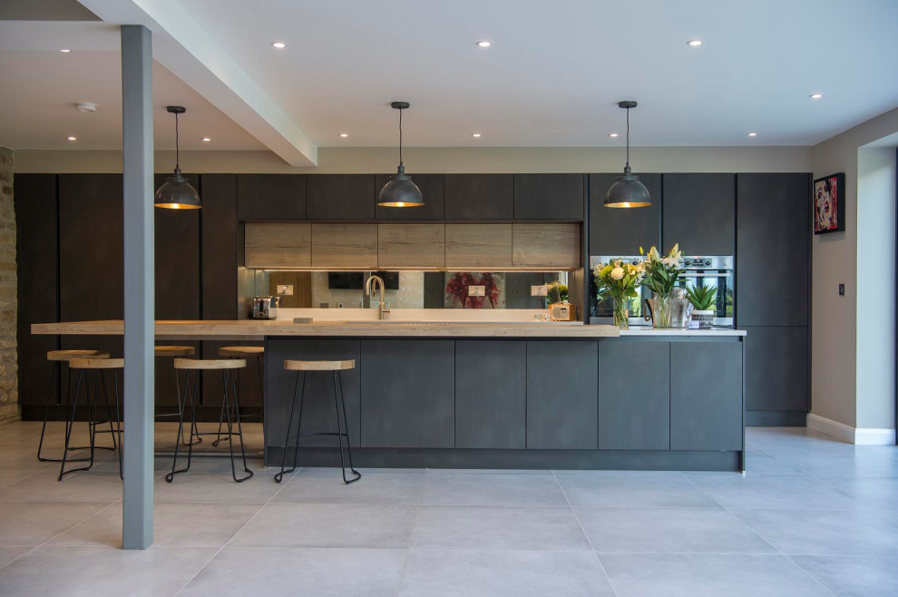 Moderne Küche mit flächenbündigen Schrankfronten, hellen Holzschränken, Arbeitsplatte aus Holz, Keramikboden, Kücheninsel und grauem Boden in Sonstige