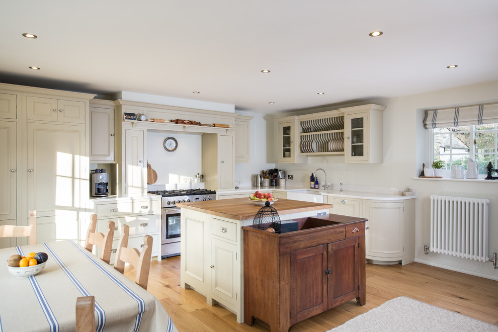 This is an example of a medium sized rural l-shaped kitchen/diner in Other with a belfast sink, recessed-panel cabinets, beige cabinets, quartz worktops, stainless steel appliances, medium hardwood flooring and an island.