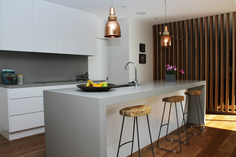 This is an example of a contemporary kitchen in Sydney with a built-in sink, white cabinets, composite countertops, grey splashback, stone slab splashback, black appliances, dark hardwood flooring, an island and grey worktops.