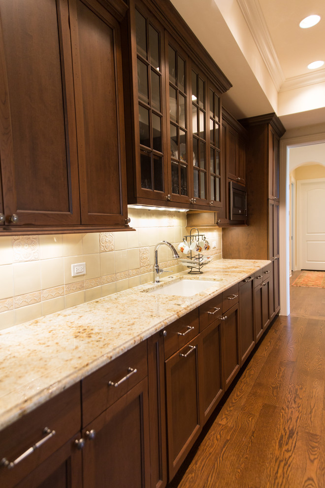 Example of a large classic l-shaped dark wood floor kitchen pantry design in Chicago with an undermount sink, recessed-panel cabinets, dark wood cabinets, granite countertops, beige backsplash, cement tile backsplash, paneled appliances and no island