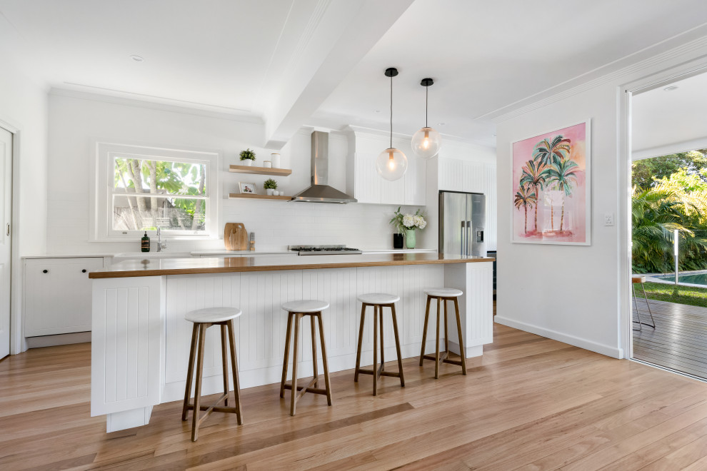 Foto de cocina marinera abierta con fregadero sobremueble, puertas de armario blancas, encimera de madera, salpicadero blanco, salpicadero de azulejos tipo metro, electrodomésticos de acero inoxidable y una isla