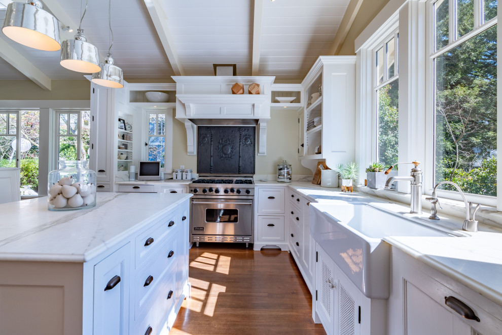 Bild på ett mellanstort lantligt vit vitt kök, med en rustik diskho, luckor med infälld panel, vita skåp, marmorbänkskiva, rostfria vitvaror, mörkt trägolv, en köksö och brunt golv