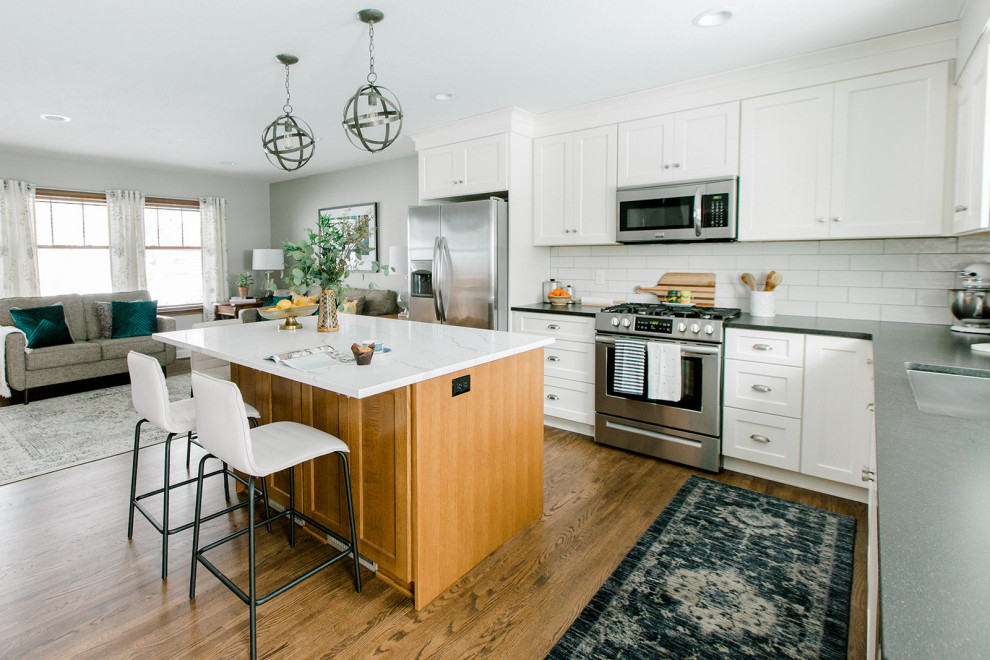 Example of a mid-sized transitional l-shaped medium tone wood floor eat-in kitchen design in Other with an undermount sink, shaker cabinets, white cabinets, quartz countertops, white backsplash, porcelain backsplash, stainless steel appliances, an island and white countertops