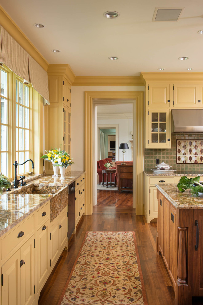 Inredning av ett klassiskt stort l-kök, med en rustik diskho, luckor med upphöjd panel, gula skåp, granitbänkskiva, flerfärgad stänkskydd, stänkskydd i keramik, rostfria vitvaror, mellanmörkt trägolv och en köksö