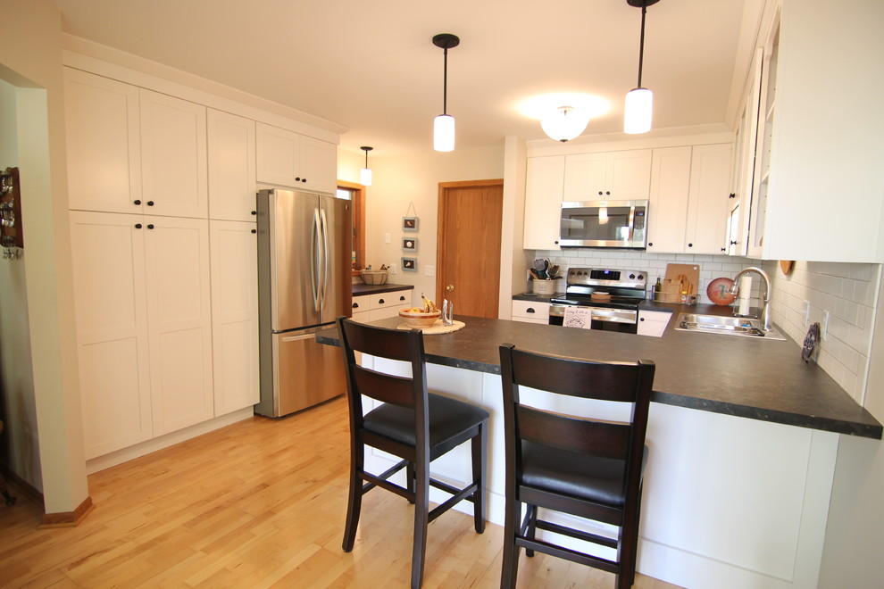 Eat-in kitchen - small cottage u-shaped light wood floor eat-in kitchen idea in Minneapolis with a drop-in sink, shaker cabinets, white cabinets, laminate countertops, white backsplash, ceramic backsplash, stainless steel appliances and a peninsula