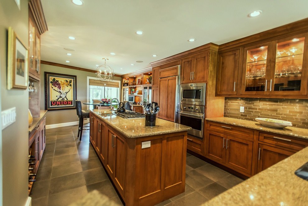 Bild på ett stort funkis kök, med skåp i shakerstil, skåp i mellenmörkt trä, granitbänkskiva, stänkskydd i stickkakel, rostfria vitvaror, en köksö, skiffergolv och grått golv