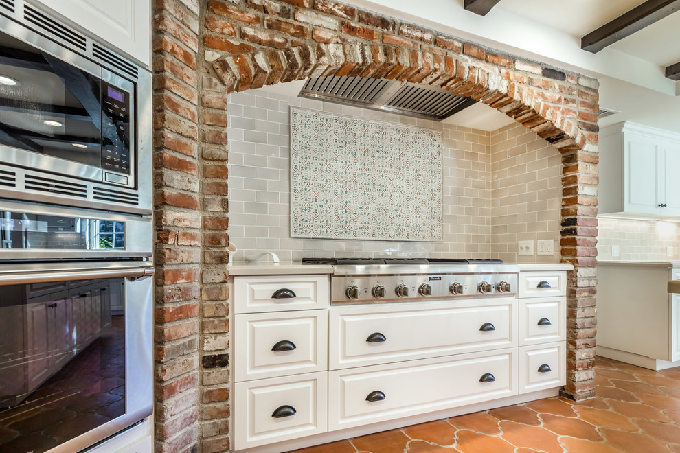 Inspiration for a large mediterranean galley terra-cotta tile and orange floor kitchen pantry remodel in Los Angeles with a farmhouse sink, raised-panel cabinets, white cabinets, quartz countertops, multicolored backsplash, porcelain backsplash, stainless steel appliances and an island