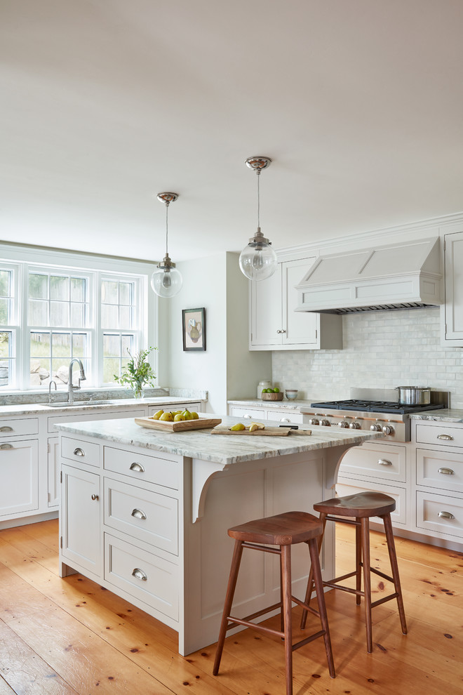 Modelo de cocinas en L tradicional con fregadero bajoencimera, armarios estilo shaker, puertas de armario blancas, salpicadero blanco, suelo de madera en tonos medios, una isla y suelo marrón