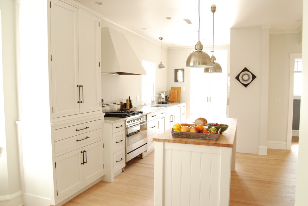 Imagen de cocina campestre con electrodomésticos de acero inoxidable, armarios con paneles empotrados, puertas de armario blancas y encimera de madera