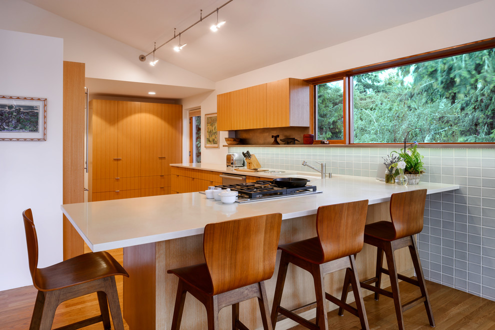 Kitchen - mid-sized 1950s l-shaped medium tone wood floor kitchen idea in Seattle with an undermount sink, flat-panel cabinets, medium tone wood cabinets, gray backsplash, a peninsula, white countertops, ceramic backsplash and stainless steel appliances