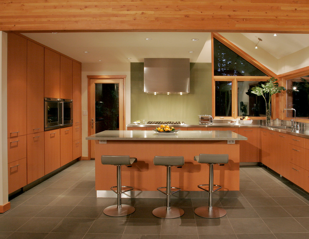 Cette image montre une cuisine design en bois brun avec un plan de travail en inox, un évier intégré, un placard à porte plane et une crédence verte.