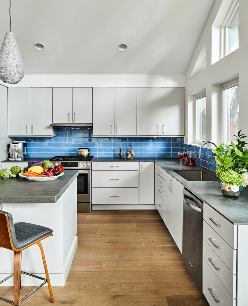 Inspiration for a large midcentury l-shaped kitchen in Austin with flat-panel cabinets, grey cabinets, engineered stone countertops, blue splashback, glass tiled splashback, stainless steel appliances, light hardwood flooring, an island, grey worktops, a single-bowl sink and beige floors.