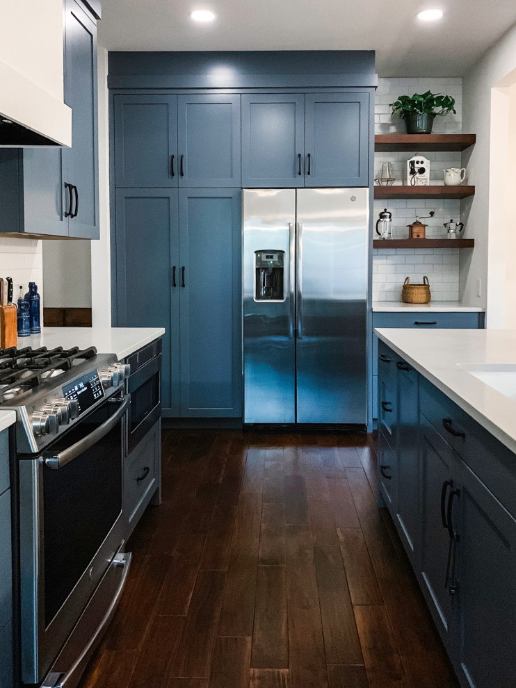 Eat-in kitchen - small transitional u-shaped dark wood floor and brown floor eat-in kitchen idea in Austin with a double-bowl sink, shaker cabinets, blue cabinets, quartz countertops, white backsplash, subway tile backsplash, stainless steel appliances, an island and white countertops