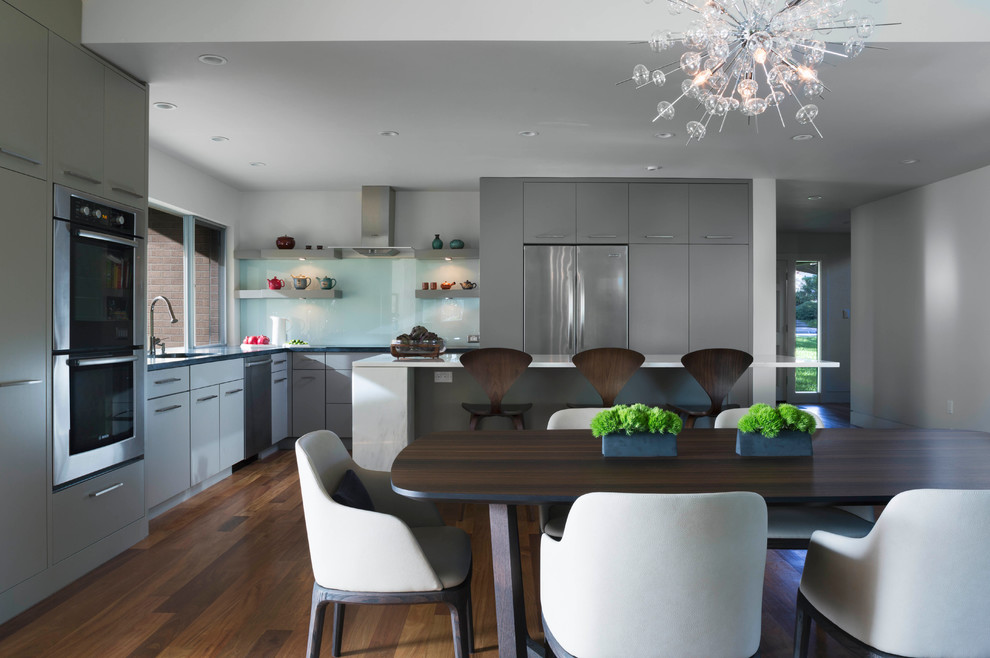 Inspiration for a large modern l-shaped medium tone wood floor eat-in kitchen remodel in Austin with flat-panel cabinets, gray cabinets, marble countertops, glass sheet backsplash, stainless steel appliances, an undermount sink and an island