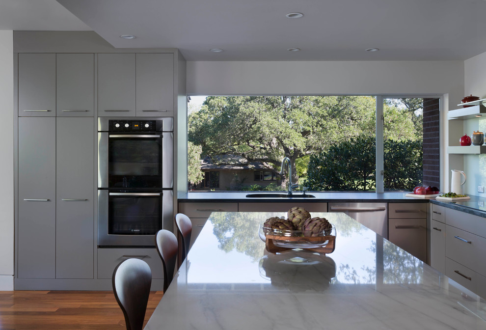 Inspiration for a large modern l-shaped kitchen/diner in Austin with a submerged sink, flat-panel cabinets, grey cabinets, marble worktops, glass sheet splashback, stainless steel appliances, medium hardwood flooring and an island.