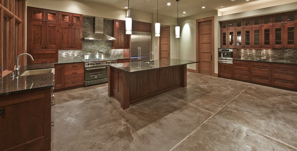 Huge trendy u-shaped concrete floor eat-in kitchen photo in Seattle with a farmhouse sink, recessed-panel cabinets, medium tone wood cabinets, granite countertops, brown backsplash, stone tile backsplash, stainless steel appliances and an island