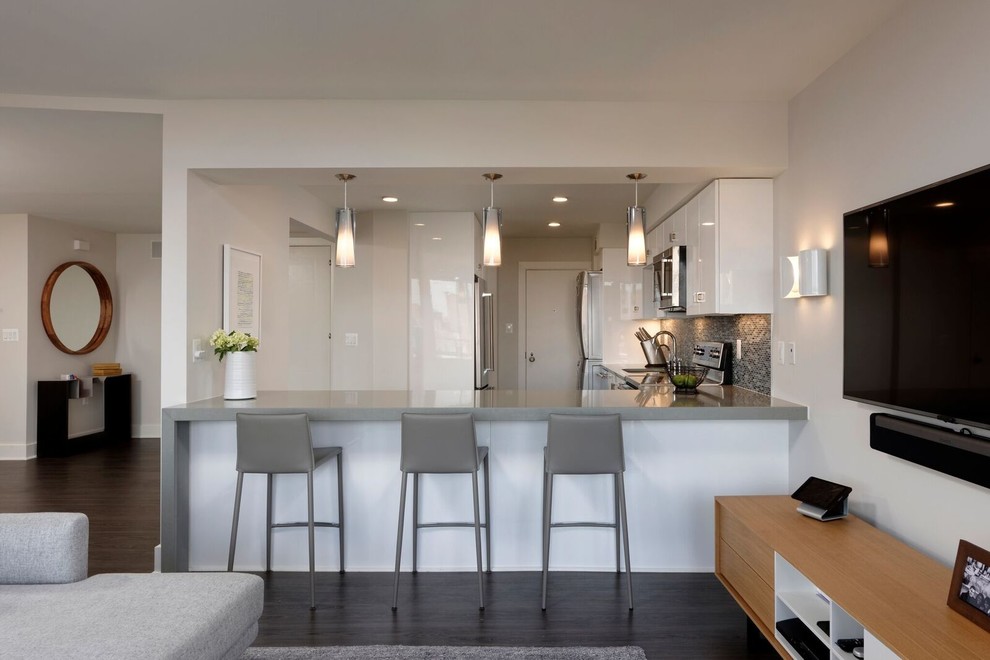 Example of a mid-sized trendy u-shaped dark wood floor eat-in kitchen design in DC Metro with an undermount sink, flat-panel cabinets, white cabinets, solid surface countertops, gray backsplash, glass sheet backsplash, stainless steel appliances and a peninsula