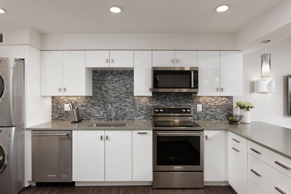 Inspiration for a mid-sized contemporary u-shaped dark wood floor eat-in kitchen remodel in DC Metro with an undermount sink, flat-panel cabinets, white cabinets, solid surface countertops, gray backsplash, glass sheet backsplash, stainless steel appliances and a peninsula