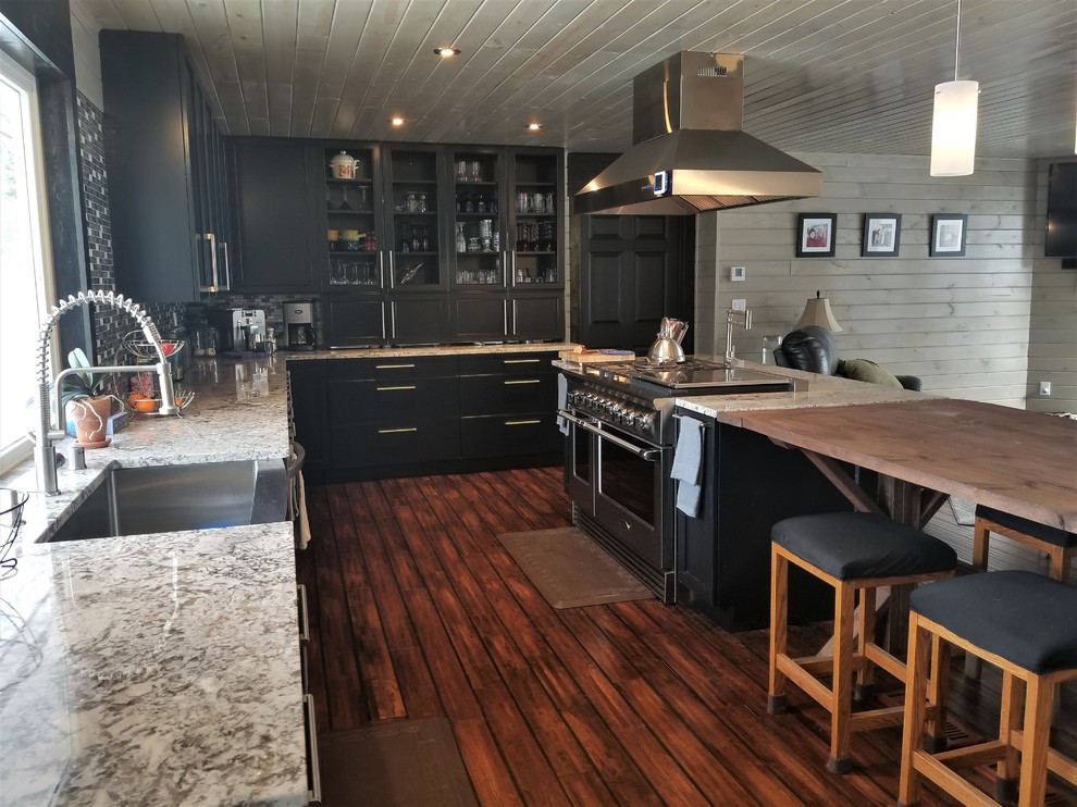 Photo of a farmhouse l-shaped open plan kitchen in Minneapolis with a belfast sink, recessed-panel cabinets, black cabinets, granite worktops, grey splashback, mosaic tiled splashback, stainless steel appliances, dark hardwood flooring and an island.