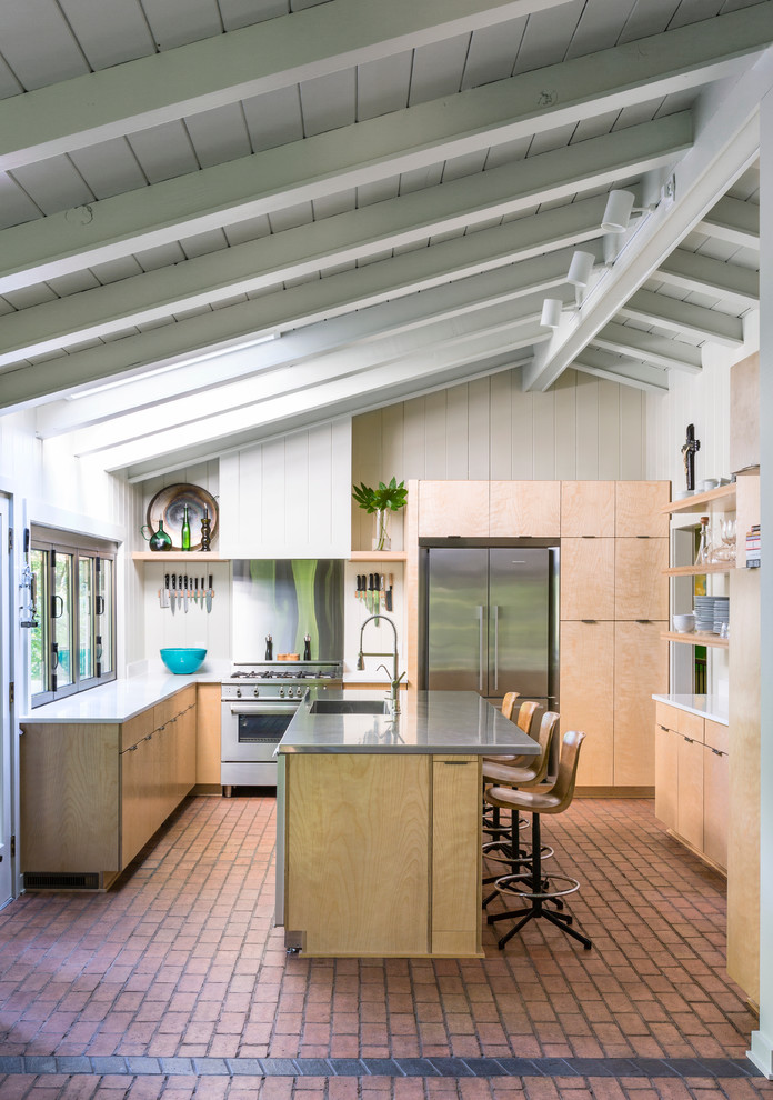Immagine di una cucina minimal con lavello integrato, ante lisce, ante in legno chiaro, elettrodomestici in acciaio inossidabile e pavimento in mattoni