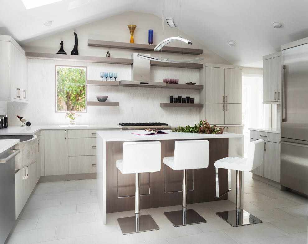 Inspiration for a contemporary u-shaped kitchen in New York with a belfast sink, flat-panel cabinets, grey cabinets, white splashback, stainless steel appliances, an island and grey floors.