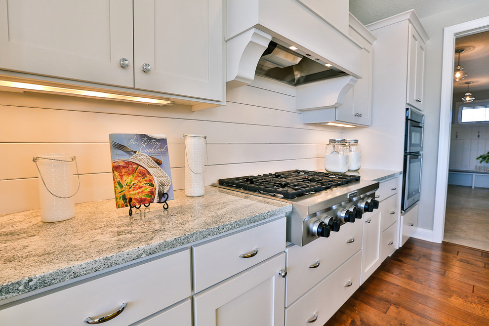 This is an example of a medium sized contemporary single-wall kitchen/diner in Minneapolis with a submerged sink, beaded cabinets, white cabinets, granite worktops, stainless steel appliances, medium hardwood flooring and an island.