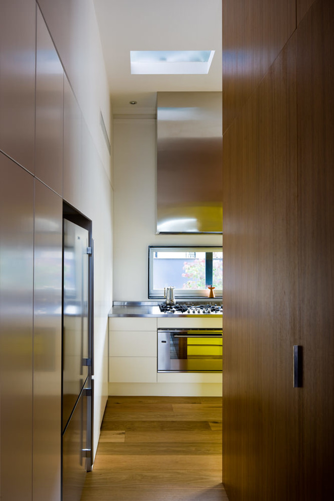 This is an example of a medium sized contemporary l-shaped kitchen pantry in Adelaide with an integrated sink, flat-panel cabinets, medium wood cabinets, stainless steel worktops, yellow splashback, glass tiled splashback, stainless steel appliances, medium hardwood flooring and no island.