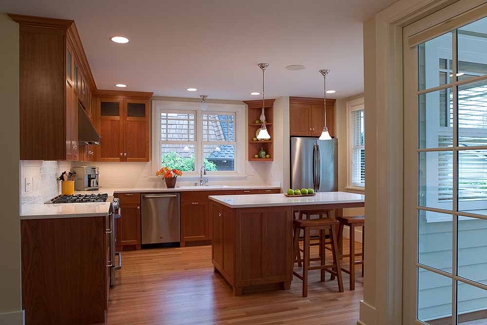 Cette photo montre une cuisine chic en L et bois brun fermée avec un électroménager en acier inoxydable, un placard avec porte à panneau encastré et une crédence blanche.