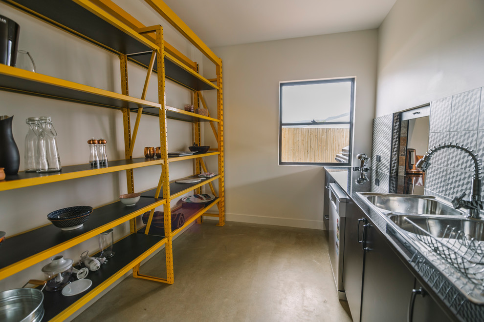 Foto di una cucina lineare industriale con lavello a doppia vasca, nessun'anta, ante gialle, top in acciaio inossidabile, nessuna isola, pavimento marrone e top grigio