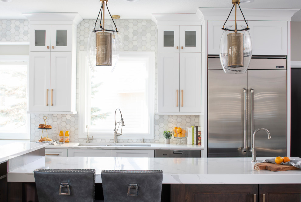 Inredning av ett klassiskt stort vit vitt kök, med en köksö, en trippel diskho, luckor med infälld panel, vita skåp, bänkskiva i kvarts, grått stänkskydd, stänkskydd i marmor, rostfria vitvaror, mellanmörkt trägolv och brunt golv