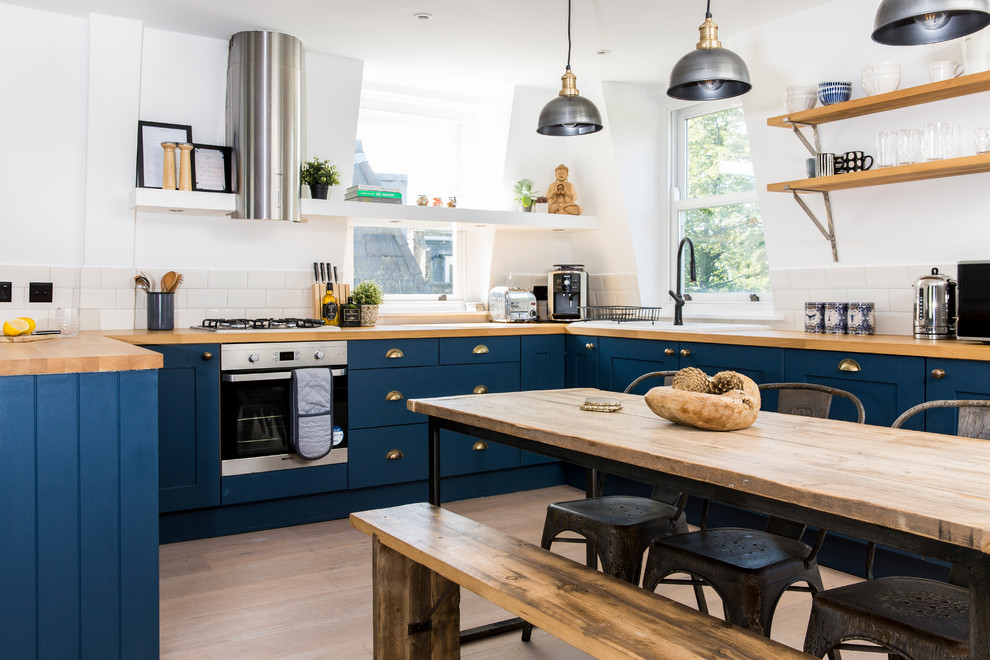 Medium sized contemporary u-shaped kitchen/diner in London with recessed-panel cabinets, blue cabinets, wood worktops, stainless steel appliances, light hardwood flooring and beige floors.