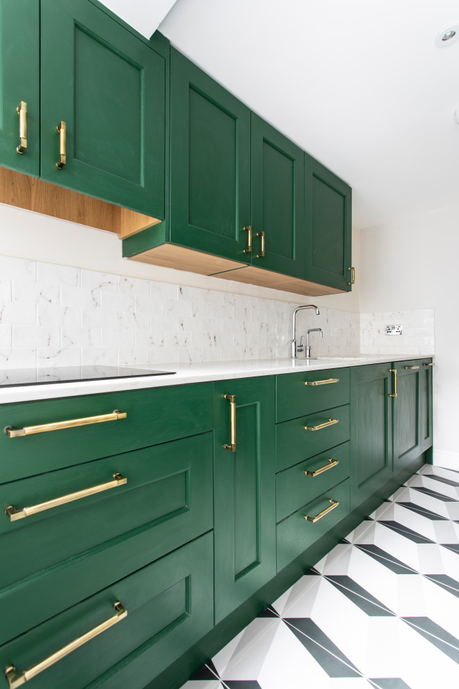 This is an example of a small contemporary galley enclosed kitchen in London with a built-in sink, shaker cabinets, green cabinets, composite countertops, white splashback, porcelain splashback, stainless steel appliances, porcelain flooring, grey floors and white worktops.