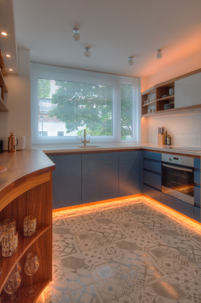 Design ideas for a medium sized contemporary u-shaped enclosed kitchen in London with a single-bowl sink, flat-panel cabinets, blue cabinets, quartz worktops, white splashback, glass sheet splashback, integrated appliances and ceramic flooring.