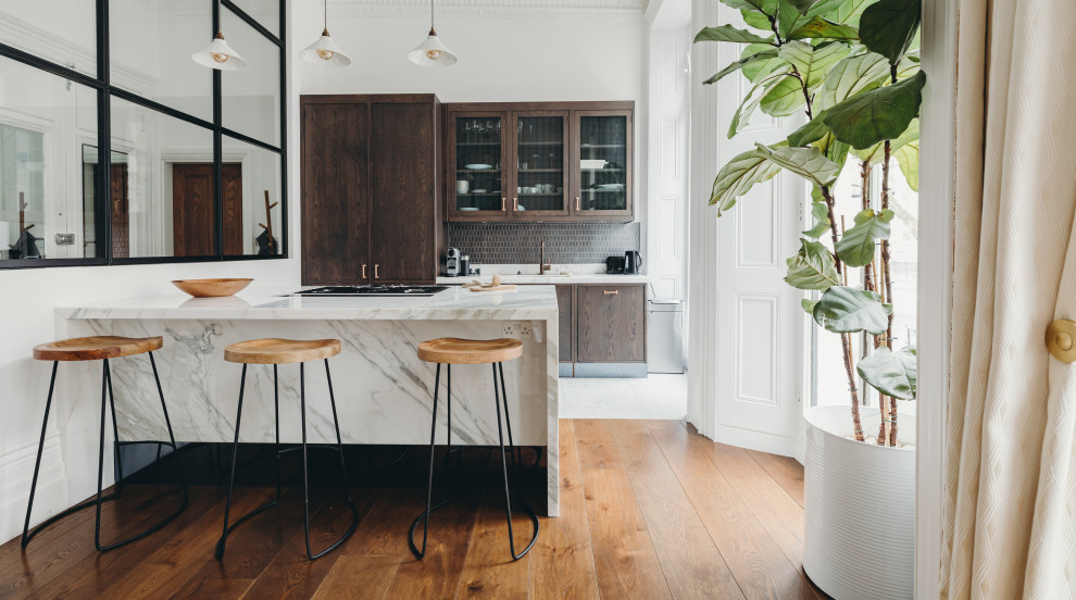 Design ideas for a medium sized contemporary galley open plan kitchen in London with a built-in sink, glass-front cabinets, dark wood cabinets, marble worktops, metallic splashback, ceramic splashback, stainless steel appliances, ceramic flooring, grey floors, white worktops and an island.