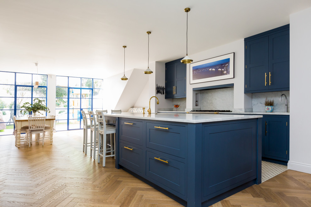 Inspiration for a traditional kitchen/diner in London with blue cabinets, marble worktops, white splashback, marble splashback, an island, white worktops, shaker cabinets, light hardwood flooring and beige floors.