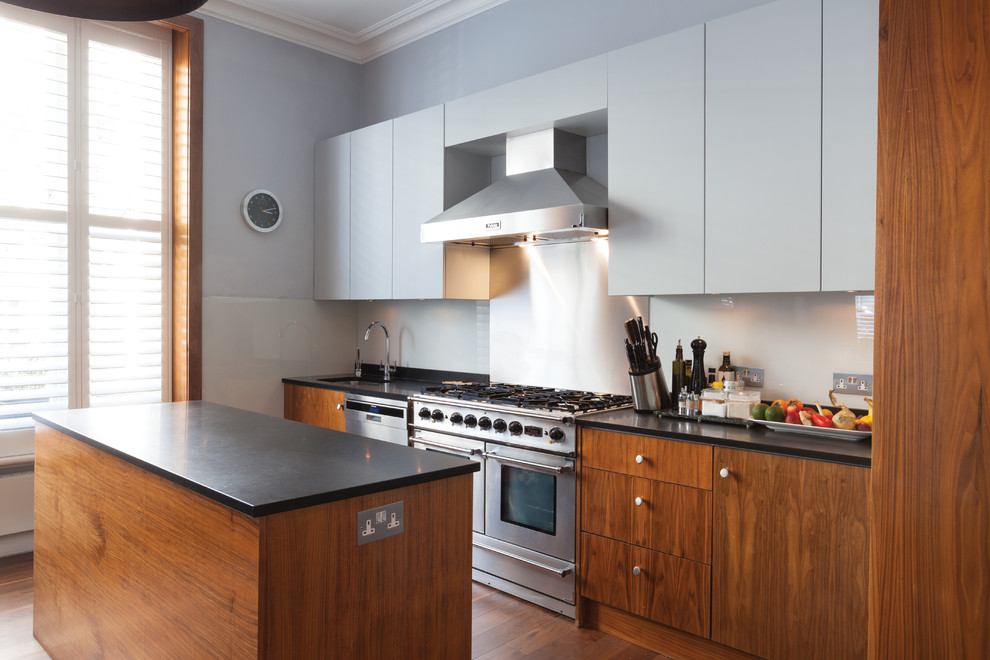 Inspiration for a medium sized contemporary galley kitchen/diner in London with flat-panel cabinets, dark wood cabinets, granite worktops, blue splashback, glass sheet splashback, stainless steel appliances, medium hardwood flooring, an island, a built-in sink and brown floors.