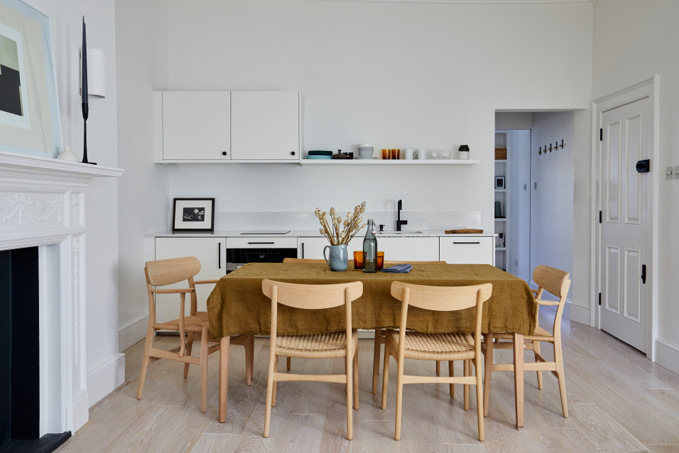 Small midcentury single-wall open plan kitchen in London with a submerged sink, flat-panel cabinets, composite countertops, white cabinets, black appliances, light hardwood flooring, no island, beige floors and white worktops.
