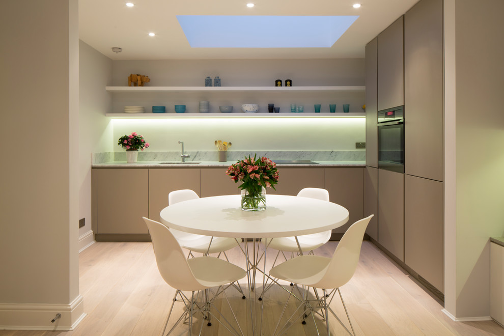 This is an example of a small modern l-shaped open plan kitchen in London with flat-panel cabinets, beige cabinets, marble worktops, light hardwood flooring, no island and white worktops.