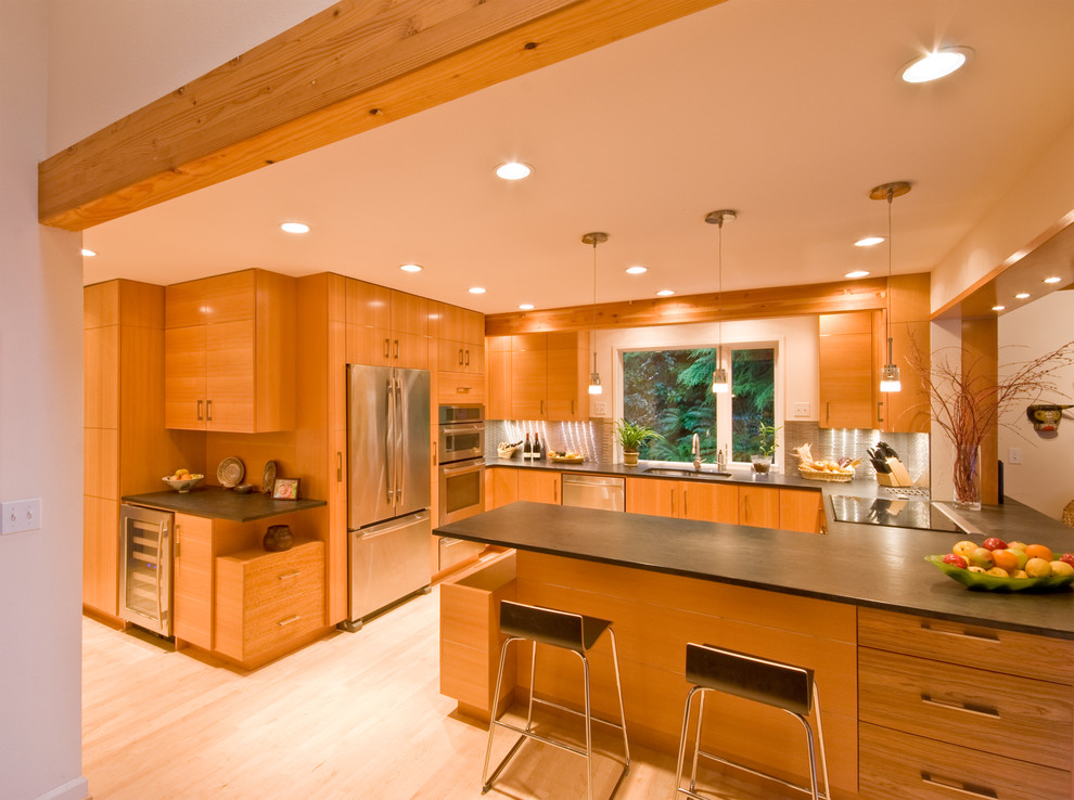 Exempel på ett modernt u-kök, med granitbänkskiva, rostfria vitvaror, släta luckor, skåp i mellenmörkt trä, stänkskydd med metallisk yta och stänkskydd i metallkakel