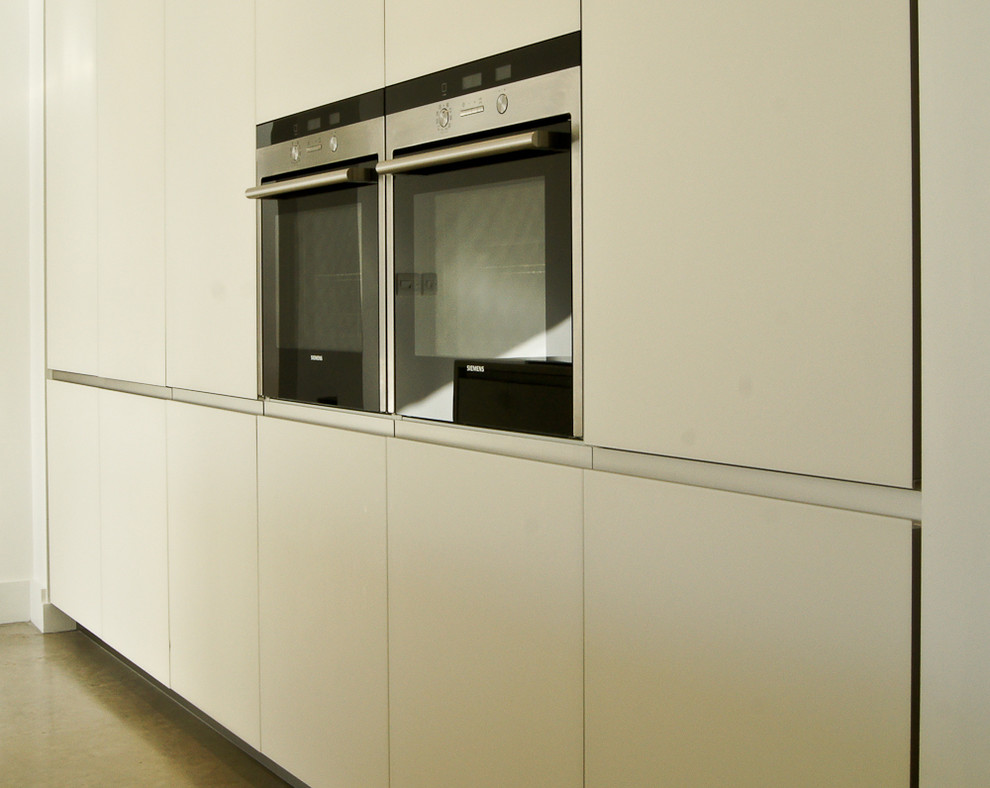 Immagine di una cucina design di medie dimensioni con lavello sottopiano, ante lisce, ante bianche, top in vetro, elettrodomestici neri e pavimento in ardesia