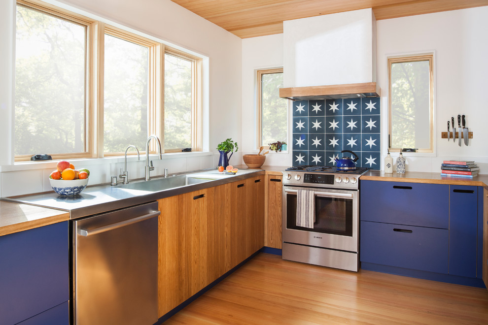 Пример оригинального дизайна: угловая кухня в скандинавском стиле с монолитной мойкой, плоскими фасадами, синими фасадами, деревянной столешницей, синим фартуком, техникой из нержавеющей стали, паркетным полом среднего тона, коричневым полом и коричневой столешницей