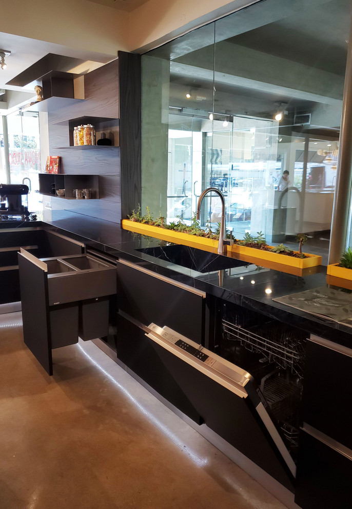 Example of a mid-sized trendy l-shaped eat-in kitchen design in Los Angeles with an integrated sink, flat-panel cabinets, black cabinets, stainless steel appliances, a peninsula and black countertops