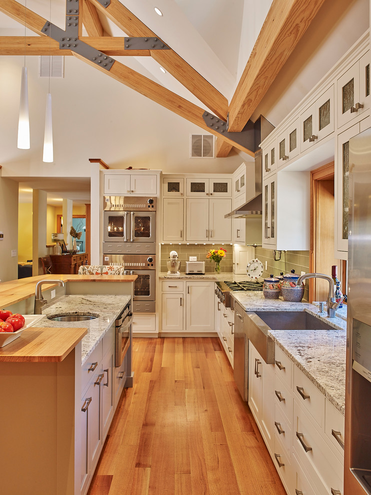 Exempel på ett klassiskt kök, med luckor med glaspanel, vita skåp, granitbänkskiva, grönt stänkskydd, stänkskydd i glaskakel, rostfria vitvaror, ljust trägolv och en köksö