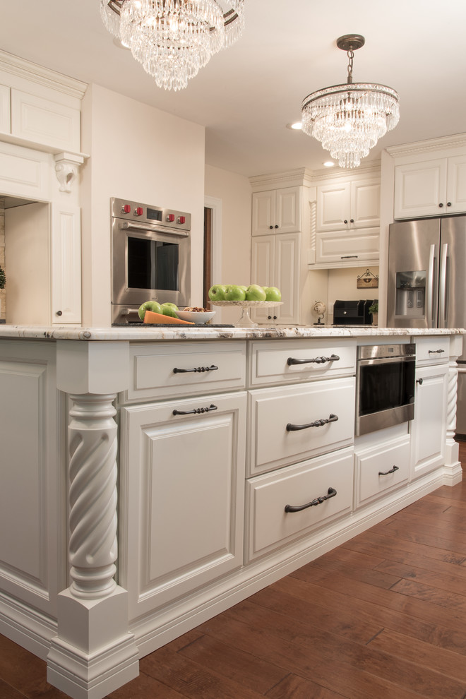 Eat-in kitchen - mid-sized traditional medium tone wood floor eat-in kitchen idea in St Louis with a farmhouse sink, raised-panel cabinets, yellow cabinets, granite countertops, beige backsplash, stone tile backsplash, white appliances and an island