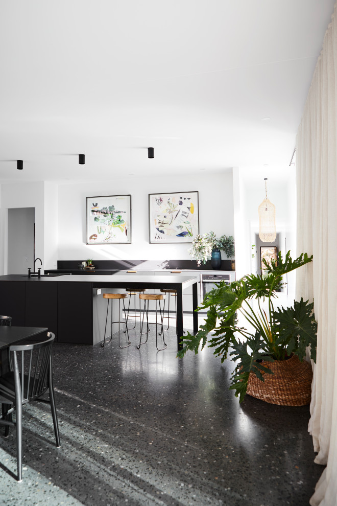 Large contemporary single-wall open plan kitchen in Other with a submerged sink, flat-panel cabinets, black cabinets, glass worktops, black appliances, concrete flooring, an island, black floors and black worktops.